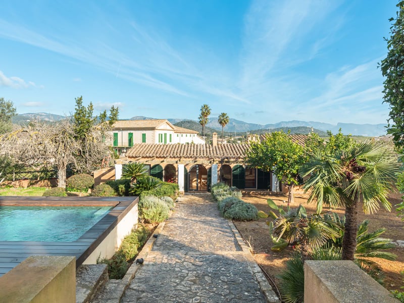 Utomhuspool och stenstig som leder till en medelhavsvilla med berg i bakgrunden.