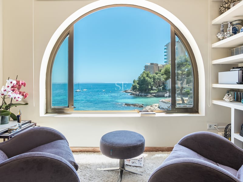 Två sammetsfåtöljer framför ett stort bågfönster med utsikt över en blå medelhavsvik med båtar.