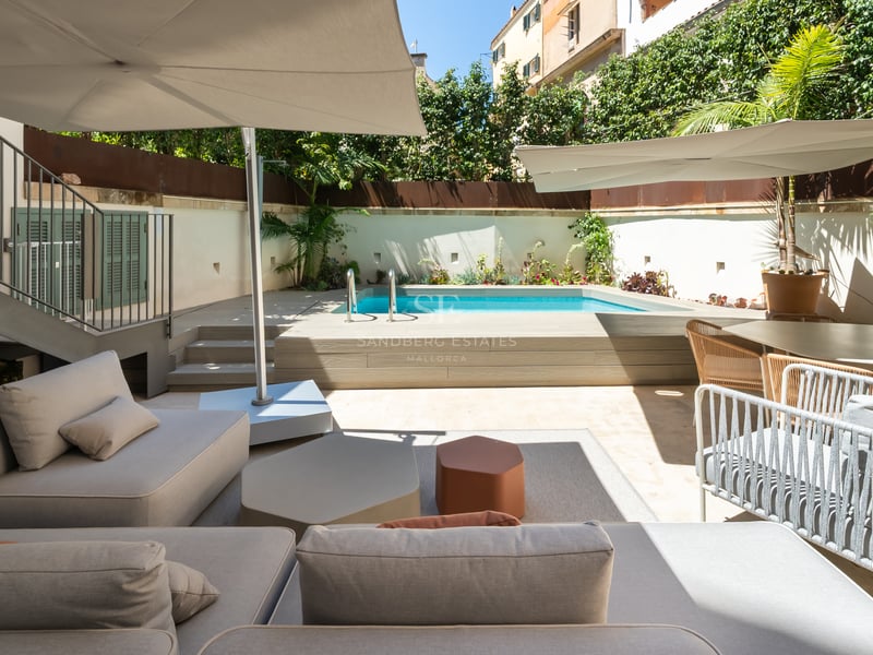 Terrasse de luxe avec canapés blancs, coin repas et piscine privée surélevée sous de grands parasols.