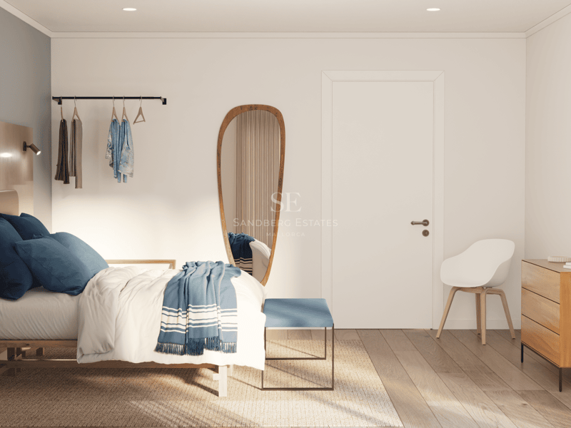 Chambre lumineuse avec un lit, des oreillers bleus, un miroir aux formes organiques et des meubles en bois clair.