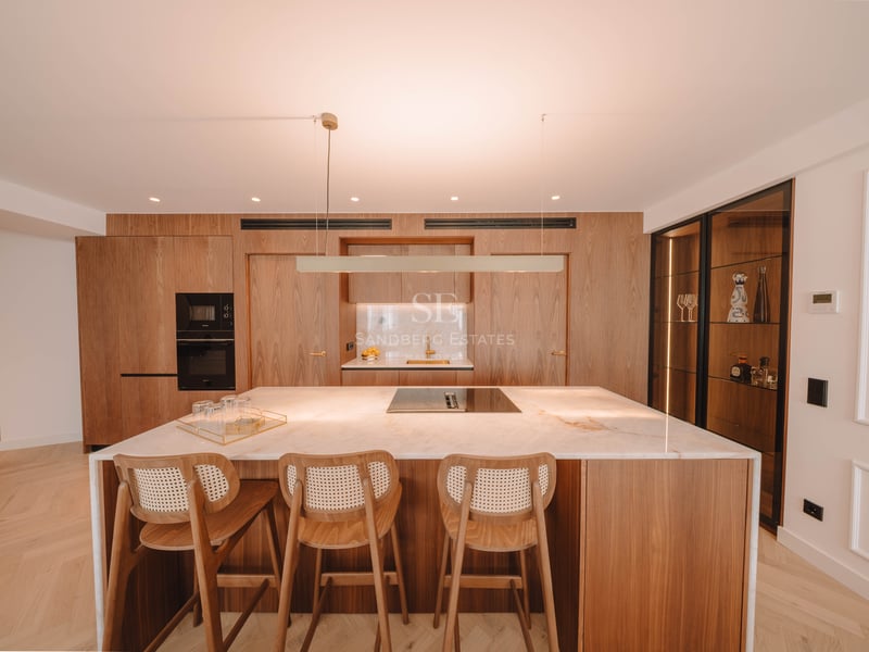 Cuisine moderne avec îlot en marbre blanc, tabourets en bois et armoires en bois sur mesure.