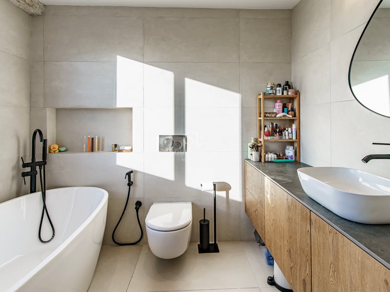 Salle de bain moderne et lumineuse avec baignoire îlot blanche, meuble sous vasque en bois et robinetterie noir mat.