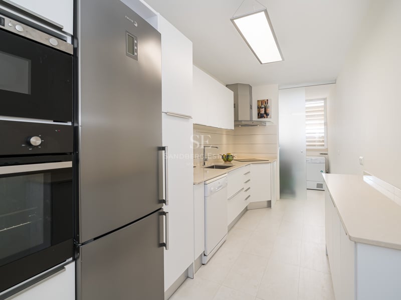 A modern galley-style kitchen with white cabinetry and stainless steel appliances.