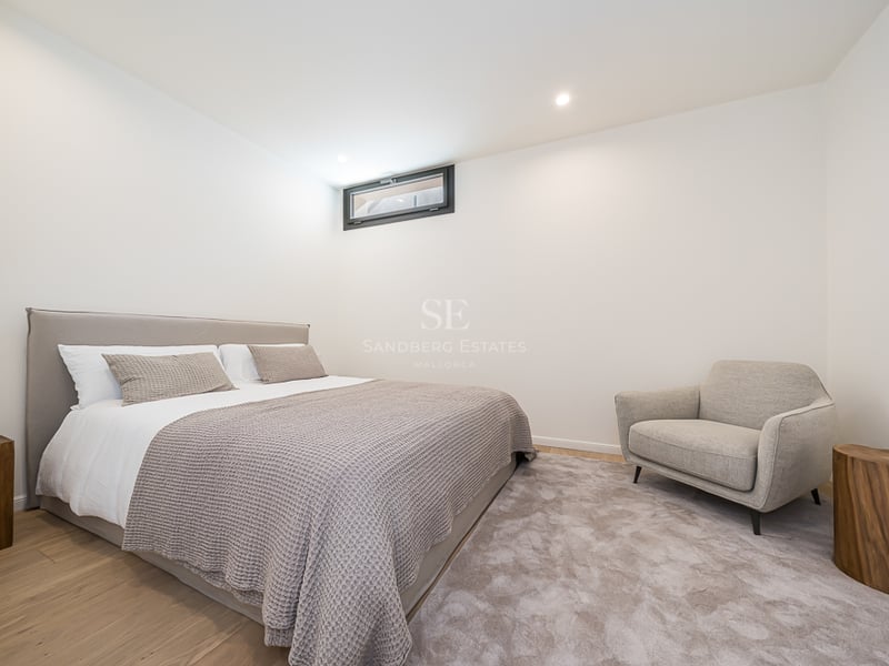 Modern bedroom featuring a double bed, grey armchair, natural wood side tables, and light oak floors.