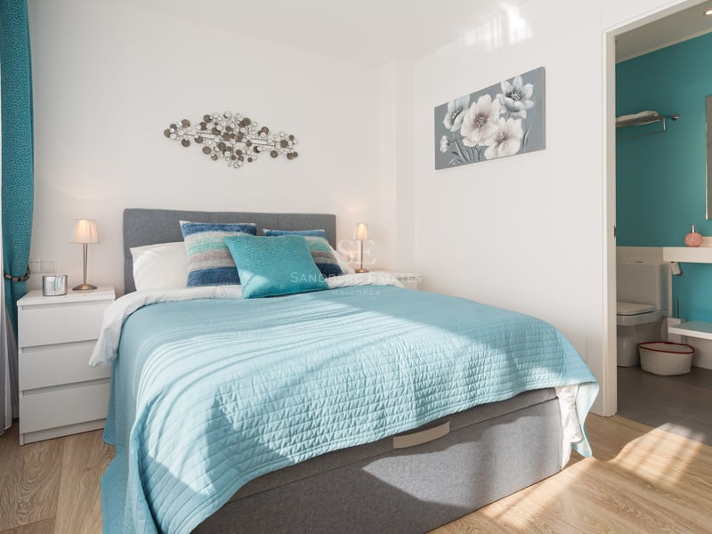Chambre lumineuse avec lit turquoise, tête de lit grise et salle de bain privative visible en arrière-plan.