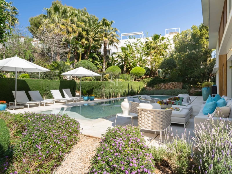 Ein heller Swimmingpool umgeben von üppigem Grün, weißen Sonnenschirmen und hochwertigen Loungemöbeln.