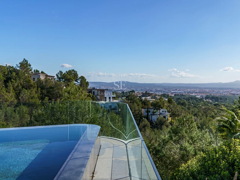 Piscine à débordement avec garde-corps en verre surplombant une vallée boisée et une ville lointaine.