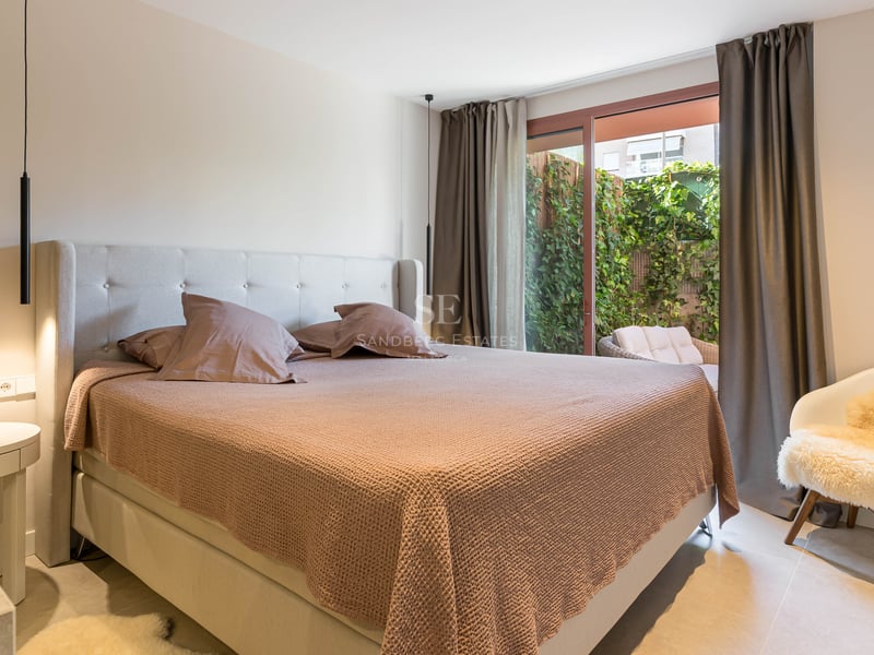 Modern bedroom featuring a king-size bed, glass sliding doors opening to a green patio, and contemporary pendant lighting.