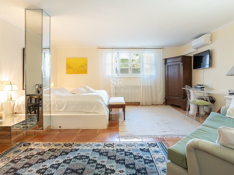 Grande chambre avec sol en terre cuite, pilier en miroir, literie blanche, armoire ancienne et coin salon.