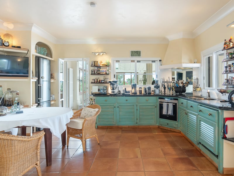Cuisine méditerranéenne avec placards turquoise à persiennes, sol en terre cuite et coin repas en osier.