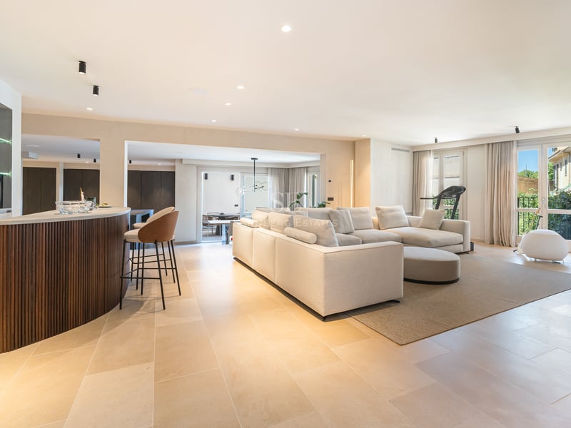 Salon moderne avec un grand canapé d'angle crème, sol en pierre naturelle et bar en bois courbé.