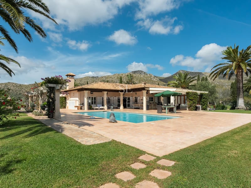Villa espagnole avec piscine rectangulaire, terrasse en terre cuite, palmiers et montagnes sous un ciel bleu.