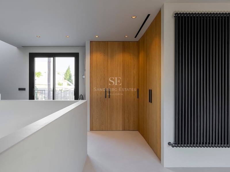 Couloir avec armoires en bois du sol au plafond, radiateur noir vertical et porte vitrée menant au balcon.