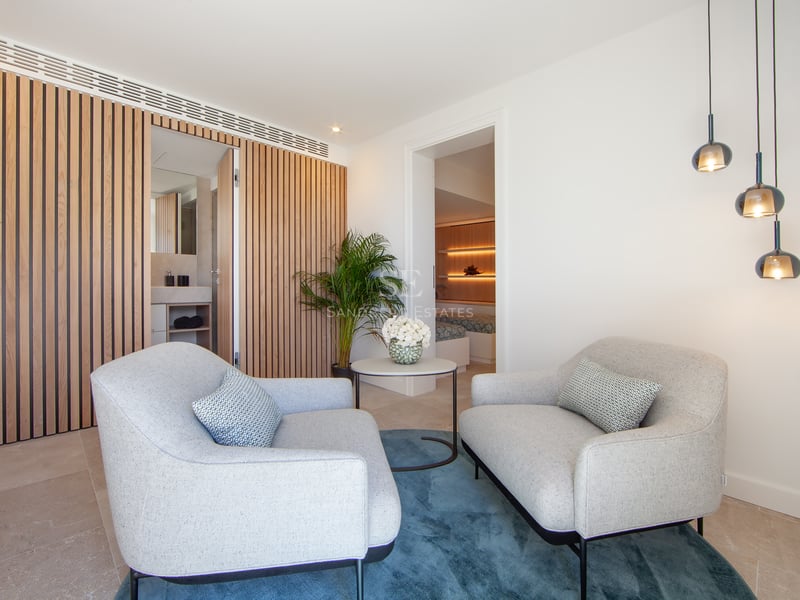 Suite parentale avec deux fauteuils gris, tapis bleu, mur en lattes de bois et vue sur la chambre.