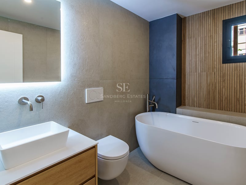 Salle de bain moderne avec baignoire îlot, vasque sur meuble en bois et miroir rétroéclairé.