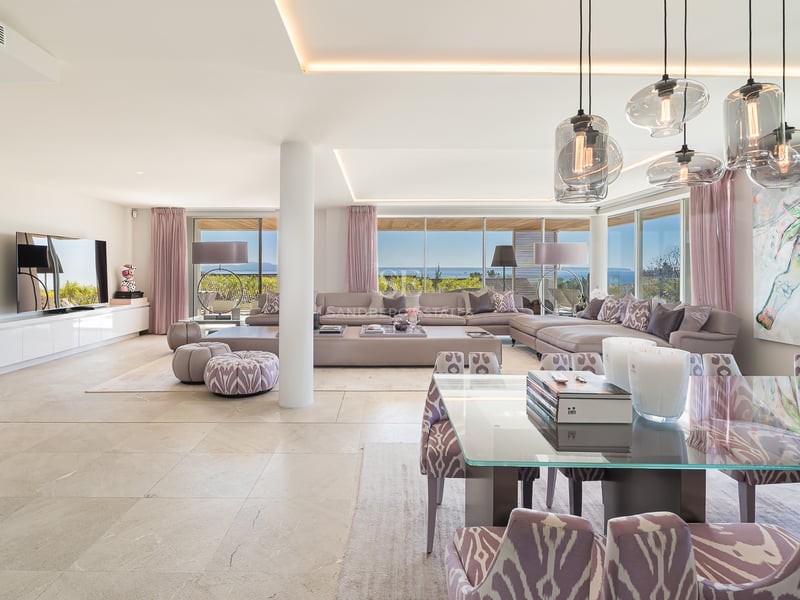 Großzügiges offenes Wohnzimmer mit modernen Polstermöbeln, Esstisch und Panoramafenstern zum Meer.