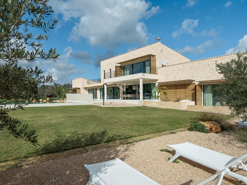 Samtida tvåvåningsvilla med naturstensväggar, stora glaspartier och gräsmatta under en blå himmel.