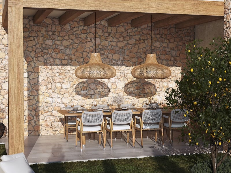 Espace repas extérieur couvert avec table en bois, suspensions en osier et mur en pierre naturelle rustique.