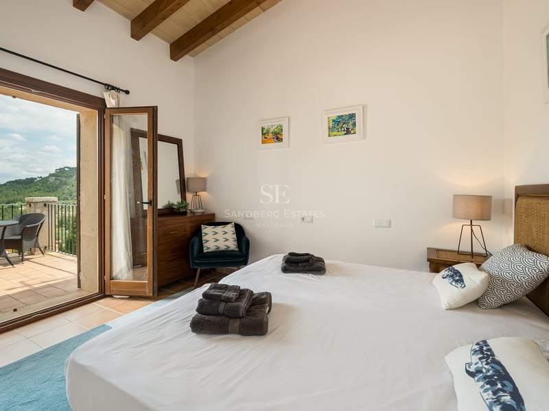 Chambre lumineuse avec poutres en bois, literie blanche et porte vitrée donnant sur une terrasse.