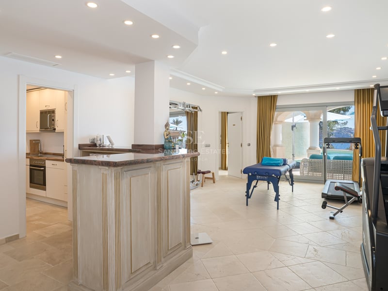 Heller Wellnessraum mit Massagetisch, Fitnessgeräten, Holzbar und Zugang zur Terrasse.