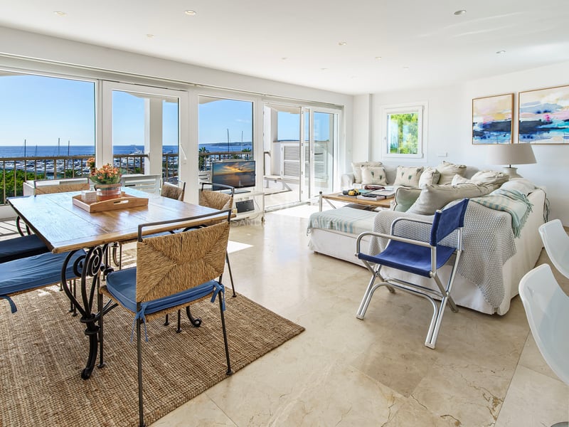 Open-plan living room with marble floors and large windows overlooking a marina and sea.