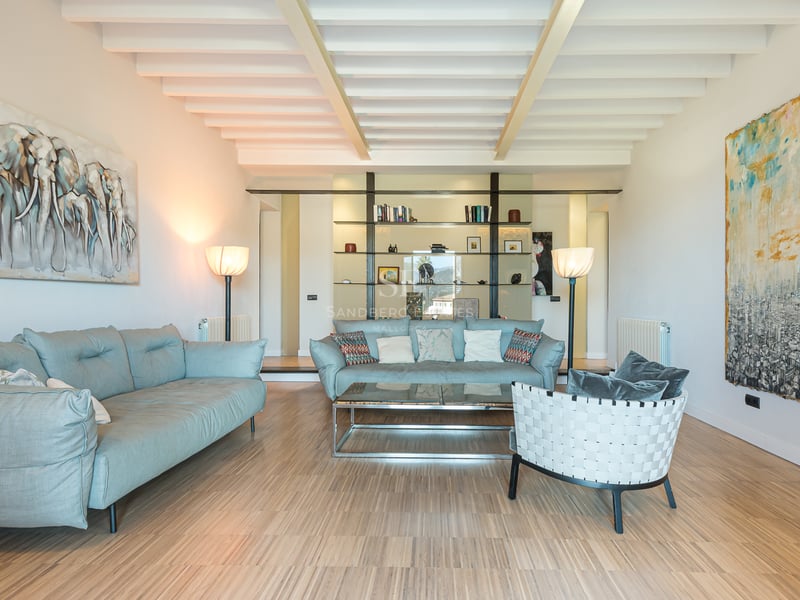 Rymligt vardagsrum med ljusblå soffor, vitt tak med bjälkar, trägolv och stora abstrakta målningar.