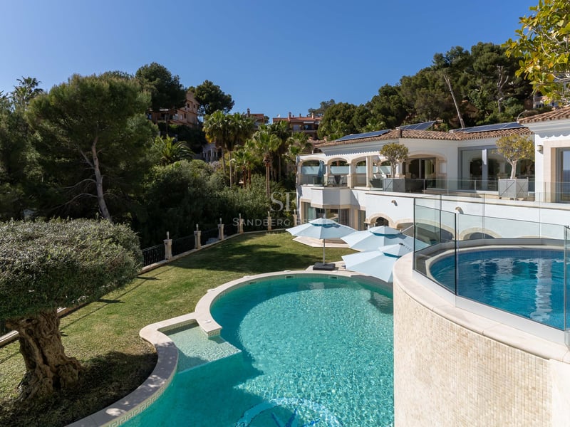 Luxusvilla mit geschwungenem türkisblauem Pool, Glasgeländern und üppigem Grün auf Mallorca.