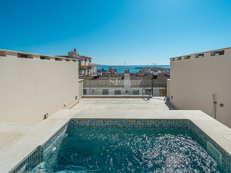 A private rooftop plunge pool with blue mosaic tiles overlooking a coastal town and harbor under a clear blue sky.