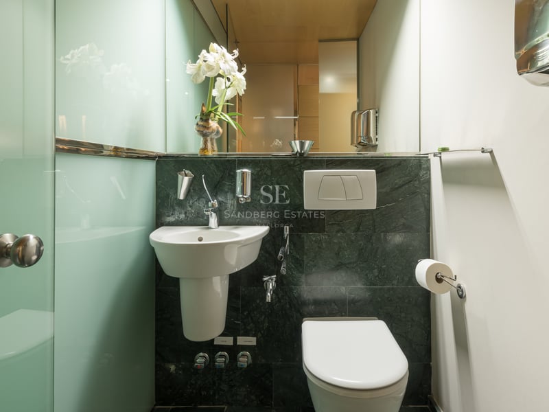 Salle de bains avec murs en marbre vert foncé, lavabo blanc et parois en verre dépoli.