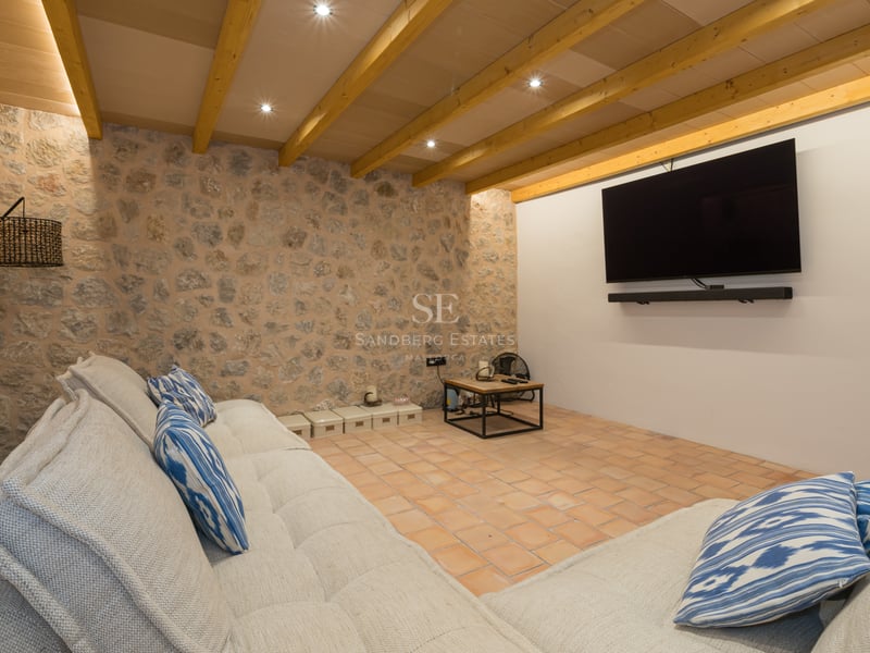 Salon multimédia rustique avec un grand canapé, télévision murale, murs en pierre et poutres apparentes.