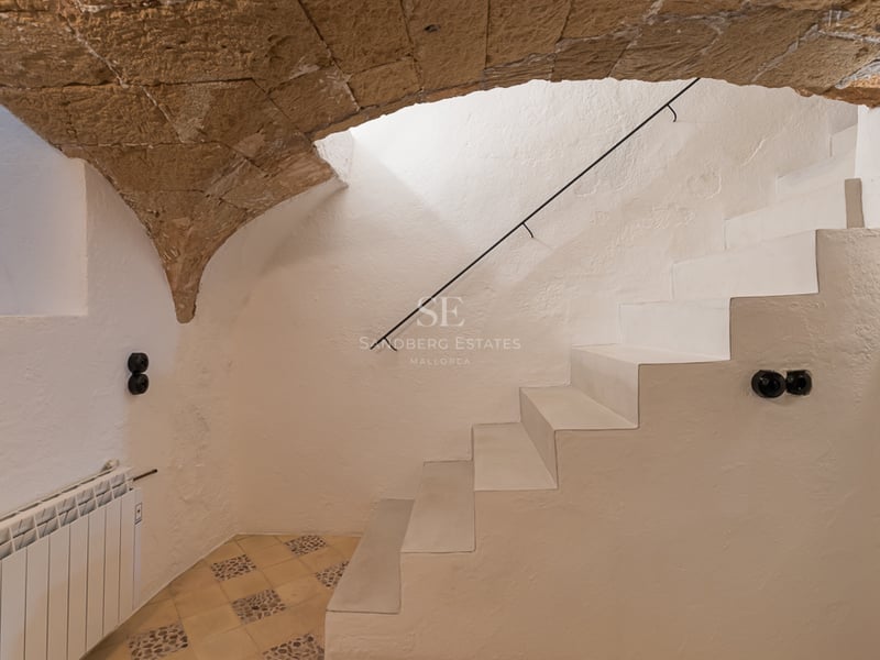 Escalier blanc minimaliste sous une voûte en pierre naturelle dans une maison rénovée à Majorque.
