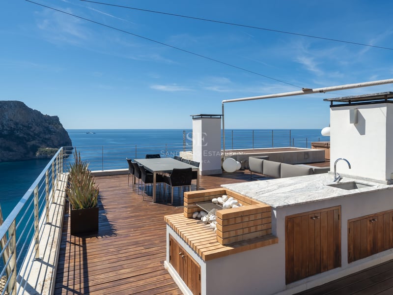 Luxury rooftop terrace featuring an outdoor kitchen, dining area, and panoramic views of a Mediterranean bay.