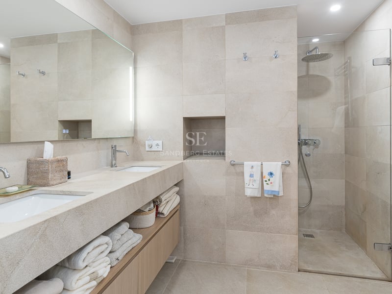 Modern bathroom featuring a double stone vanity, wood cabinets, and a walk-in glass shower with beige tiling.