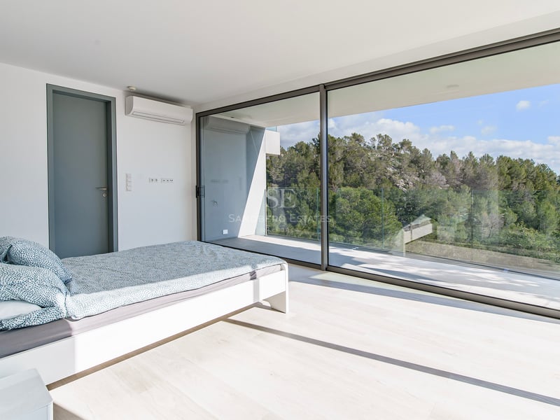 Chambre lumineuse avec baies vitrées ouvrant sur un balcon surplombant une forêt verdoyante.
