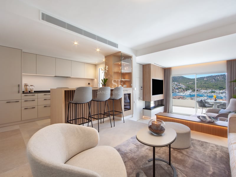 Salon et cuisine ouverts et modernes avec des armoires beiges et une grande fenêtre donnant sur un port de plaisance.