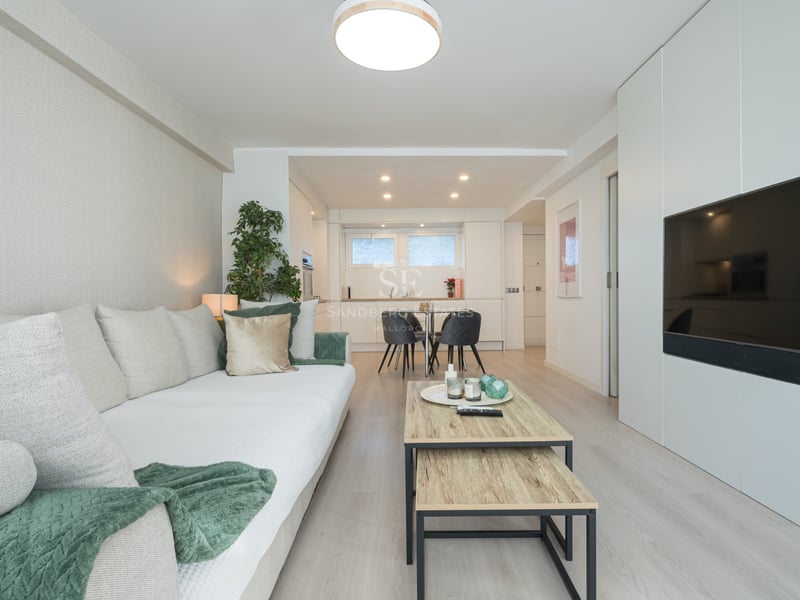 Bright modern living room featuring a white sofa, light wood floors, and a large flat-screen TV integrated into white cabinetry.