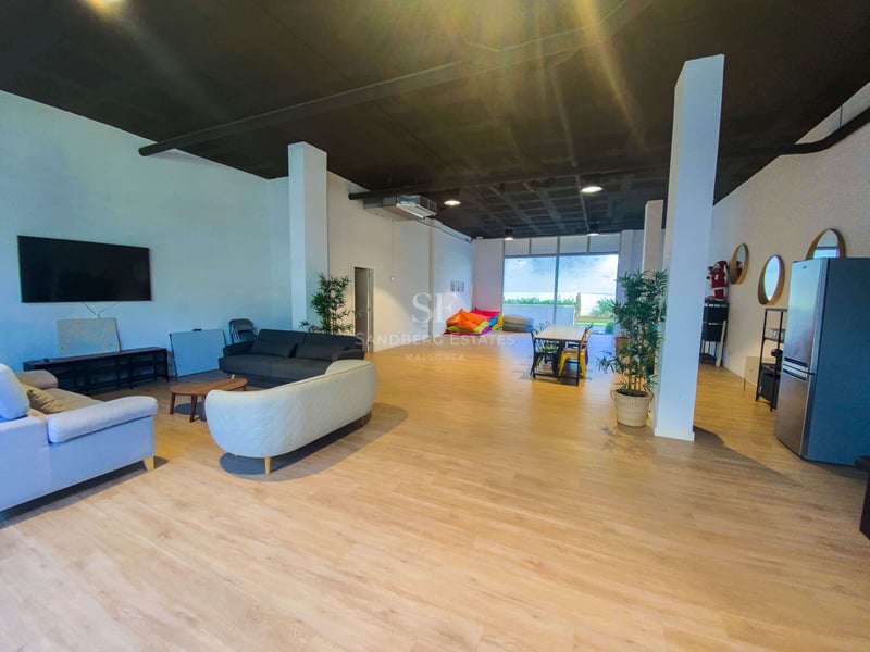 Großer offener Raum mit hellem Holzboden, Sofas, Esstisch, bunten Sitzsäcken und Zugang zum Garten.