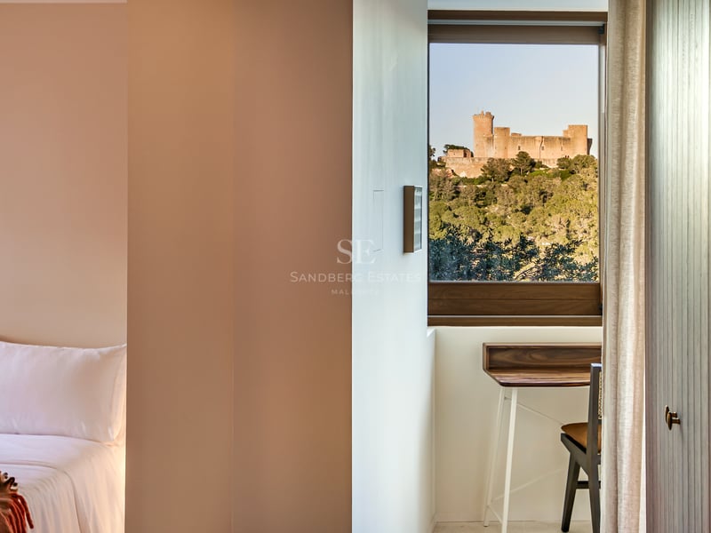 Modernes Schlafzimmerfenster mit Blick auf eine mittelalterliche Burg auf einem bewaldeten Hügel und einem Schreibtisch.