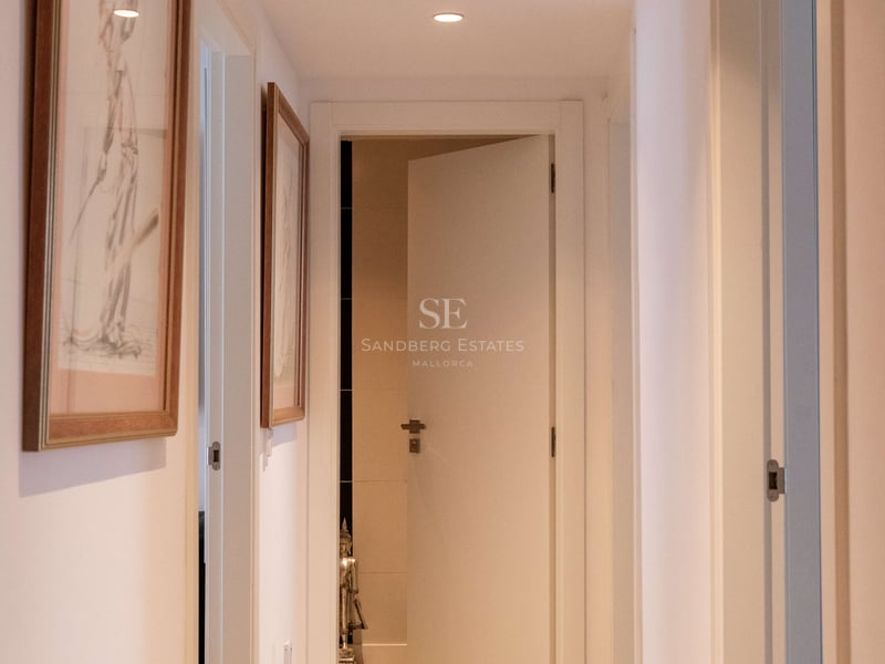 Moderner weißer Flur mit Einbaustrahlern und hellem Holzboden, der zu einer offenen Tür führt.