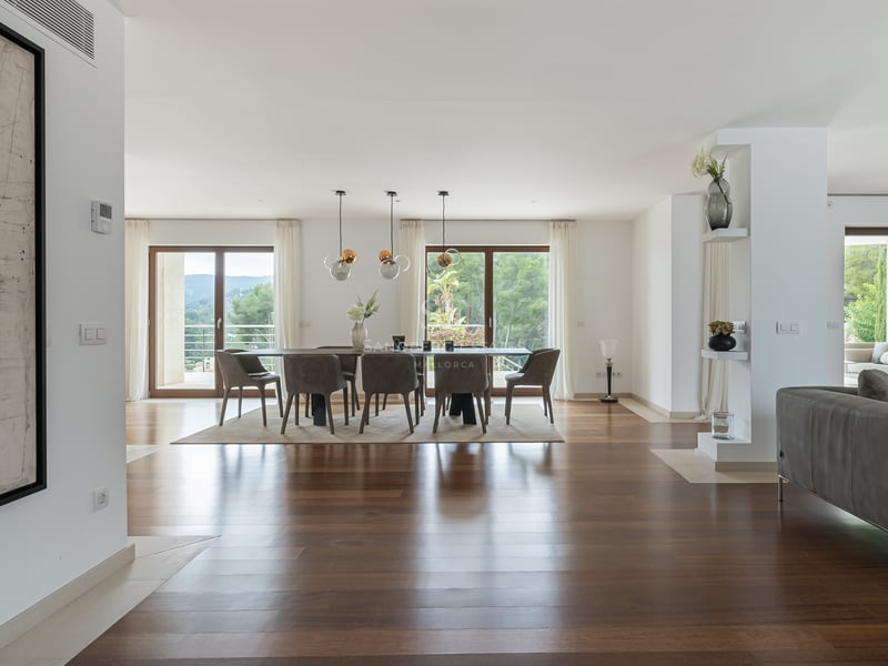 Salle à manger spacieuse avec parquet sombre, suspensions design et baies vitrées donnant sur un jardin verdoyant.