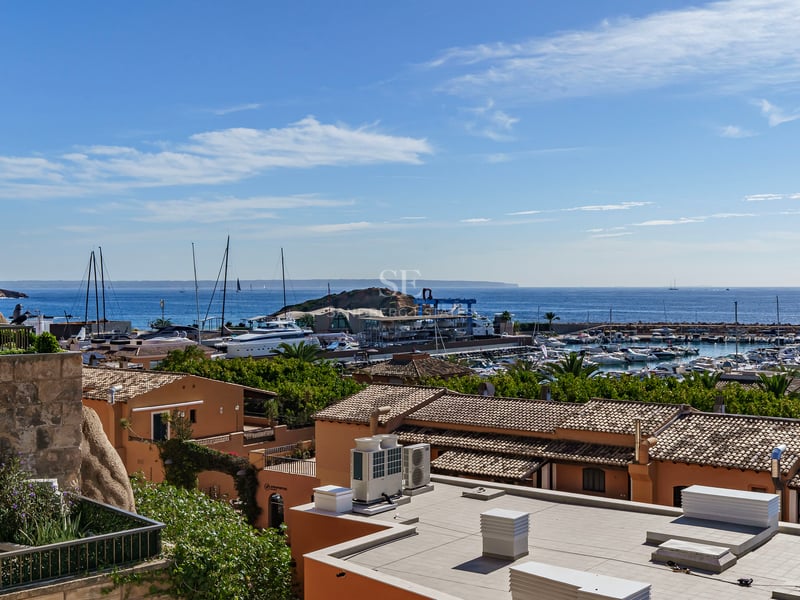 Elevated view of a Mediterranean marina with terracotta roofs, white yachts, and the blue sea under a clear sky.