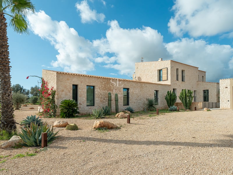 Naturstensfasad på en modern villa med kaktusträdgård och grusuppfart under en klarblå himmel.