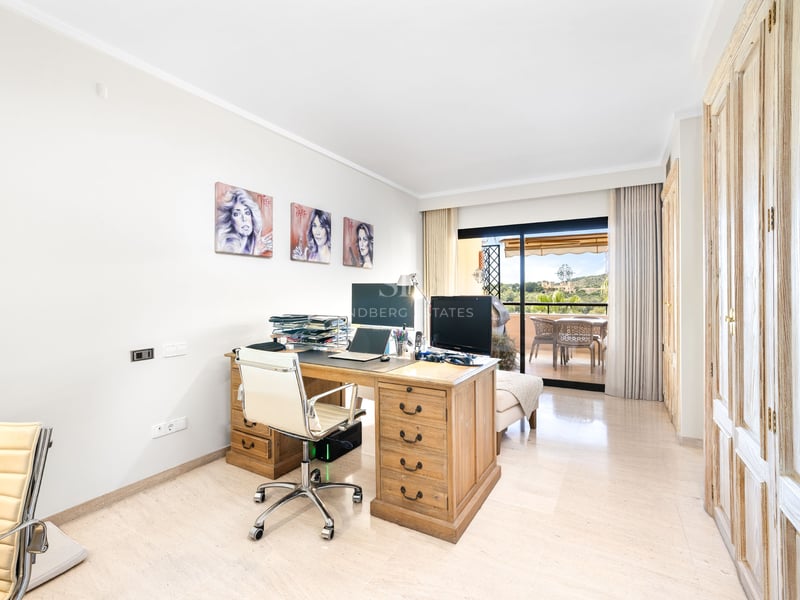 Bureau lumineux avec grand bureau en bois, chaise blanche et baies vitrées ouvrant sur une terrasse.