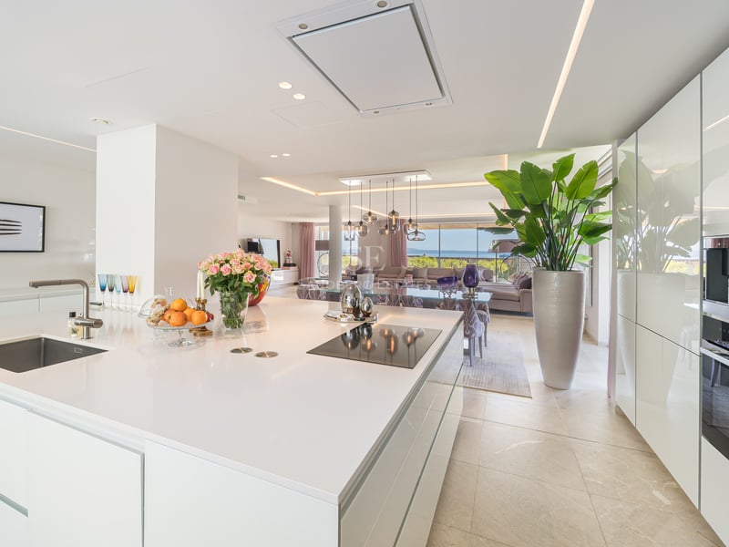 Weiße Kücheninsel mit Induktionskochfeld, mit Blick auf das Wohnzimmer und das Mittelmeer im Hintergrund.