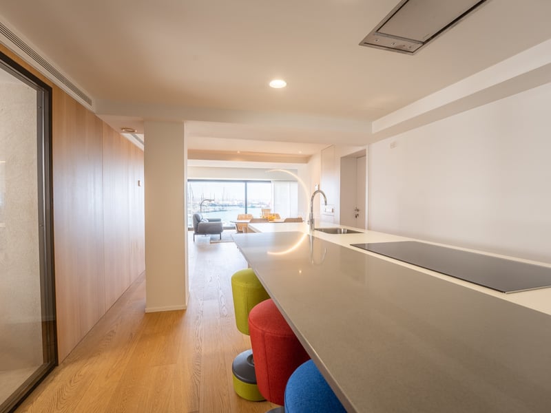 Köksö med färgglada pallar som leder till ett vardagsrum med utsikt över en marina genom fönster.