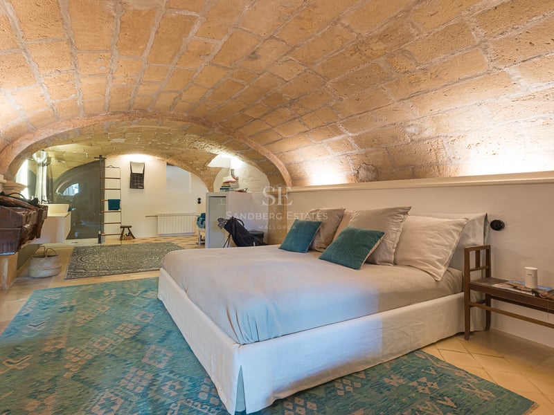 Chambre avec plafond voûté en grès, murs blancs, tapis turquoise et lit moderne.