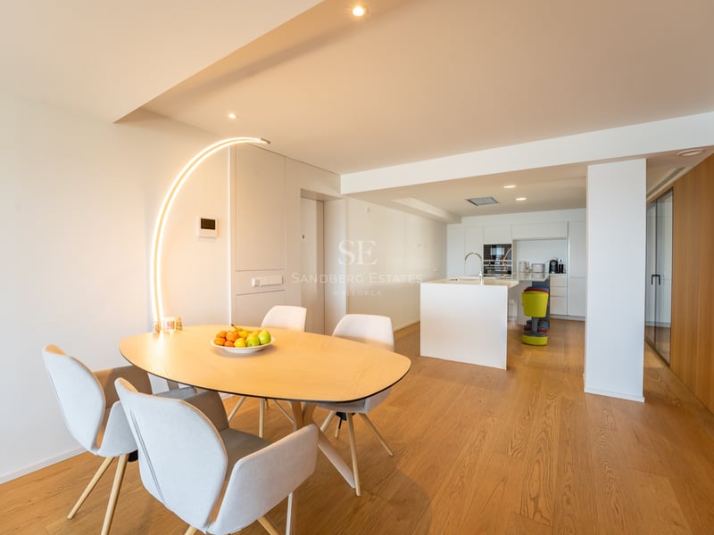 Minimalistisk matplats med bord i ljust trä, grå stolar och en iögonfallande båggolvlampa.