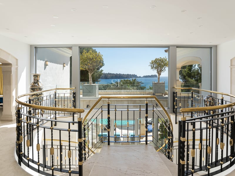 Innenansicht eines Marmortreppenhauses mit kunstvollem Geländer und Blick durch große Fenster auf das Meer.