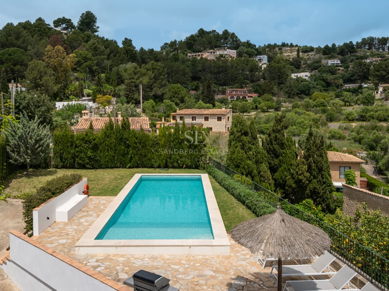 Piscine rectangulaire turquoise entourée d'une terrasse en pierre naturelle et de verdure avec vue sur la montagne.