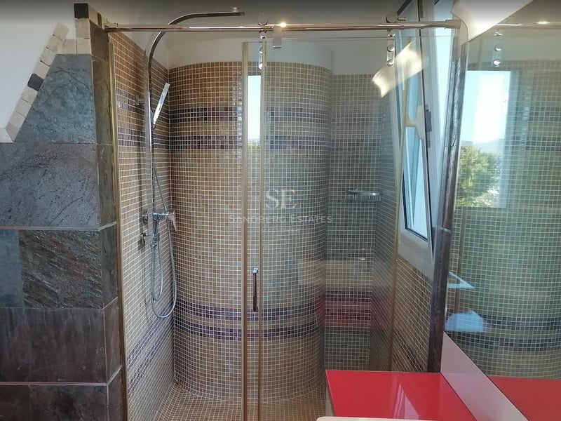 Une cabine de douche en verre avec des carreaux de mosaïque beiges, une robinetterie chromée et un mur courbe.